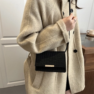 Elegant black croco-effect crossbody bag with gold accents shown on a beige winter coat
