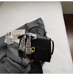 Détail du sac carré en cuir noir avec boucle dorée et un foulard imprimé noir et blanc