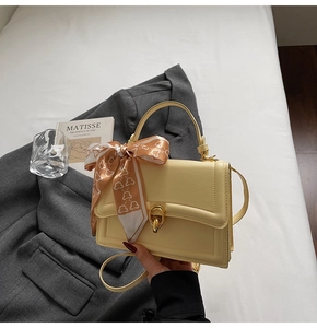 Détail du sac bandoulière en cuir jaune avec fermoir tournant doré et foulard en soie