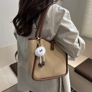 Minimalist cream tote bag with brown straps and plush charm worn by a model