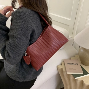 Détail d'un sac à bandoulière tressé bordeaux avec pendentif feuille porté par un mannequin