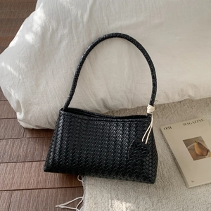Detail of black woven leather underarm bag with a cute heart charm and braided strap