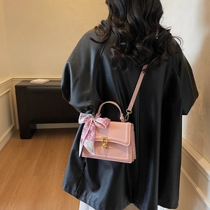 Sac à bandoulière en cuir rose avec fermoir doré et foulard en soie porté par un mannequin
