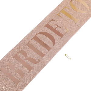 Close-up of glittery rose gold Bride to Be sash with metallic pin for wedding parties