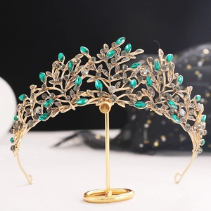 Elegant gold baroque bridal crown with green marquise gems and grey crystals on a stand