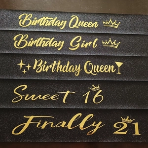 Detailed close-up of various black glitter birthday sashes with gold foil lettering