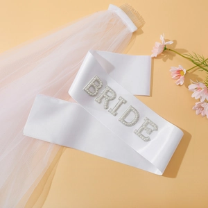 Close-up of white satin Bride sash with pearl lettering and bridal veil on comb