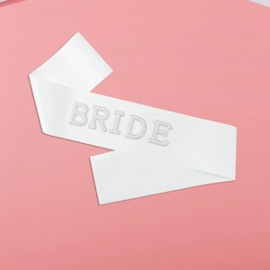 Close-up of white satin Bride sash with pearl lettering on a pink background