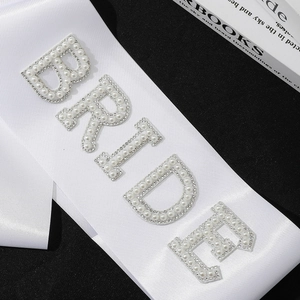 White bridal sash with pearl and rhinestone BRIDE lettering on a minimalist black background