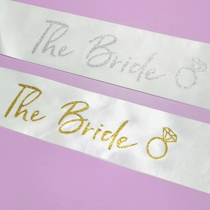 Détail de rubans en satin blanc avec lettrage pailleté The Bride doré et argenté et icônes