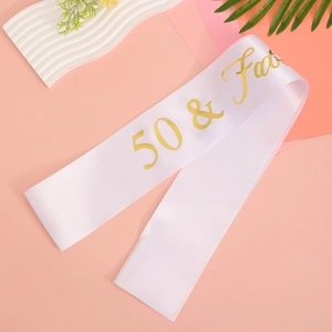 White satin 50 & Fab birthday sash with gold lettering on a decorative background