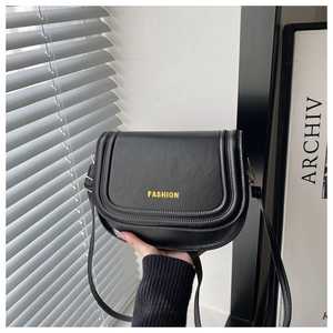 Detail view of black crossbody bag featuring a curved flap with FASHION text and piping