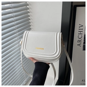 Detailed view of white saddle bag featuring gold FASHION lettering and stitching