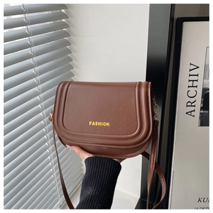 Close-up of brown saddle bag with golden FASHION logo and premium stitching details