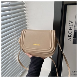 Detail of beige saddle bag featuring gold FASHION lettering and adjustable strap