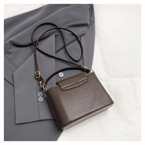 Détail d'un sac à main structuré en cuir marron foncé avec finitions dorées sur un blazer