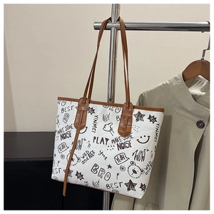 Detail of white tote bag featuring black graffiti bear prints and brown leather straps