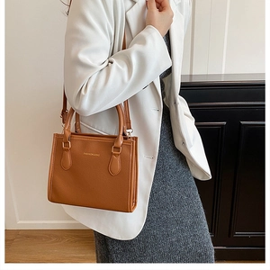 Detail of a brown lychee pattern tote bag with gold hardware worn by a model in a white blazer