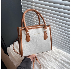 Detail of white lychee leather tote bag with brown handles and gold printed slogan