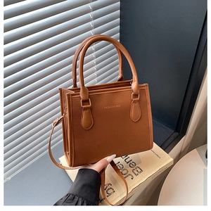 Detailed macro view of caramel lychee leather texture and golden embossed logo on tote bag