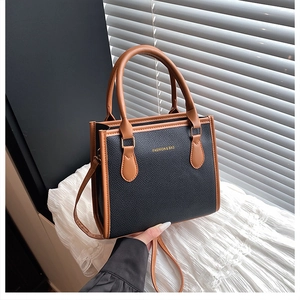 Close-up of contrast stitching on black and brown leather tote with gold fashion lettering