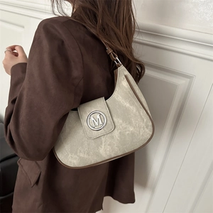 Retro cream faux suede underarm bag with brown trim and silver M logo on model