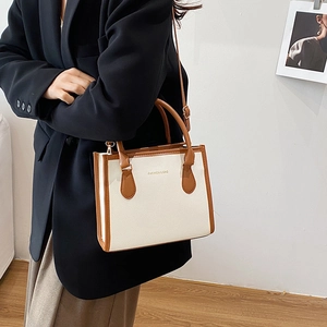 White textured leather tote bag with brown handles, shown worn by a model in a suit