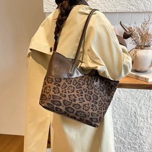 Large leopard print tote bag with brown leather trim carried by a model in a trench coat