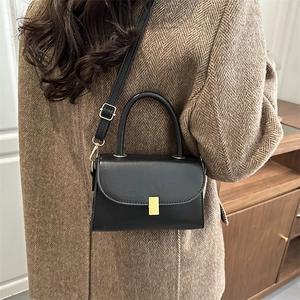 Sac bandoulière minimaliste en cuir noir avec boucle dorée sur manteau d'hiver