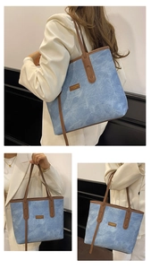 Detail view of a blue textured tote bag with brown leather handles and brand logo patch
