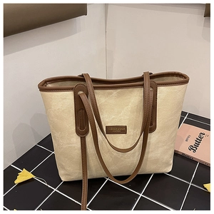 Detail view of beige canvas tote bag with brown leather trim on checkered surface