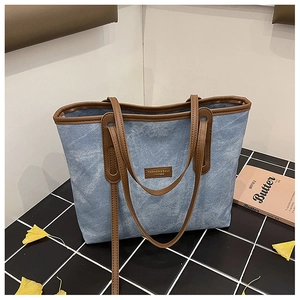 Detail shot of blue denim tote bag featuring brown leather trim and fashion logo patch