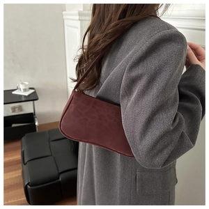 Detailed close-up of a burgundy leopard embossed suede baguette bag worn with a grey blazer