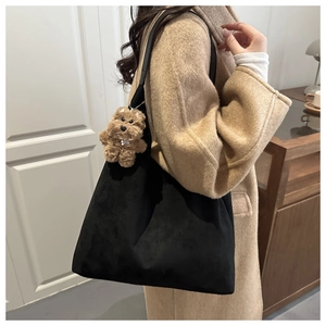 Close-up of black matte tote bag featuring a cute plush dog pendant charm on shoulder