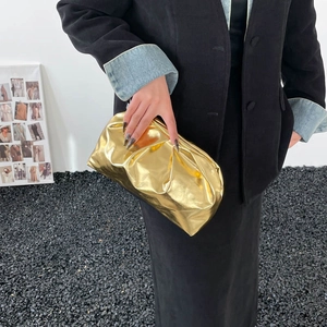 Chic gold pleated cloud clutch bag with metallic finish held by model on black gravel