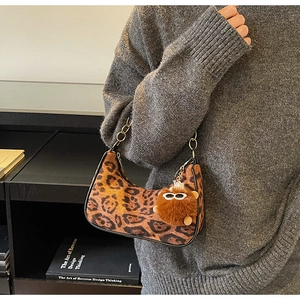 Detail of leopard print hobo bag with fuzzy pendant and chain strap on shoulder