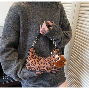 Close-up of leopard print crescent bag with stylish plush bear charm and metal chain