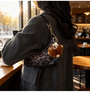 Detailed close-up of grey leopard print saddle bag with a cute plush doll charm