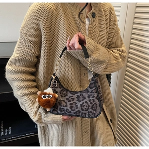 Detail of leopard print crescent bag featuring a plush monster charm and gold chain
