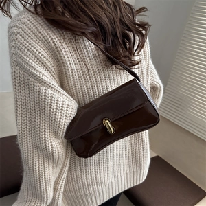 Glossy dark brown PU leather shoulder bag with gold metal clasp on a model in beige sweater