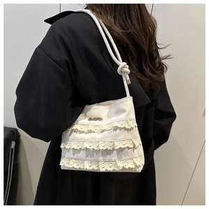 Detail of cream lace bucket bag with plaid fabric and ruffled layers worn over black coat