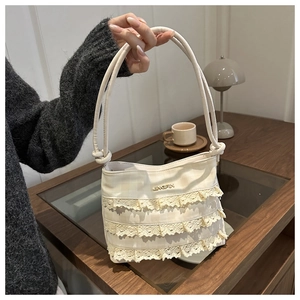 Detail of elegant cream lace layers on a textured tote bag with golden metal logo