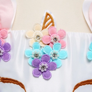 Dettaglio ravvicinato di fiori ricamati e unicorni su un abito da bambina in raso bianco