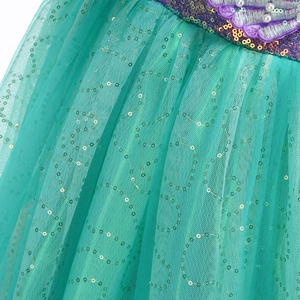 Détail d'une robe en tulle vert avec paillettes dorées, broderie violette et perles