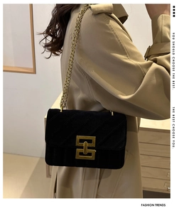 Close-up of black velvet shoulder bag with gold geometric lock and chain on khaki coat