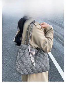 Detail of grey quilted tote bag with woven shoulder straps and plush charm in outdoor setting