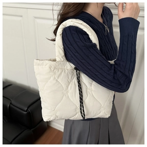 Detail of white quilted tote bag featuring heart embroidery and woven drawstring closure