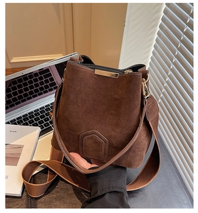 Macro view of brown suede bucket bag featuring golden metal trim and sleek crossbody strap
