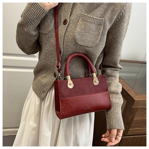 Detail of burgundy two-tone crossbody bag with woven handle and gold hardware