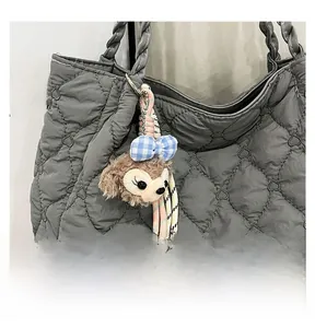 Detail view of pink plush charm with blue plaid bow and colorful woven strap on a bag